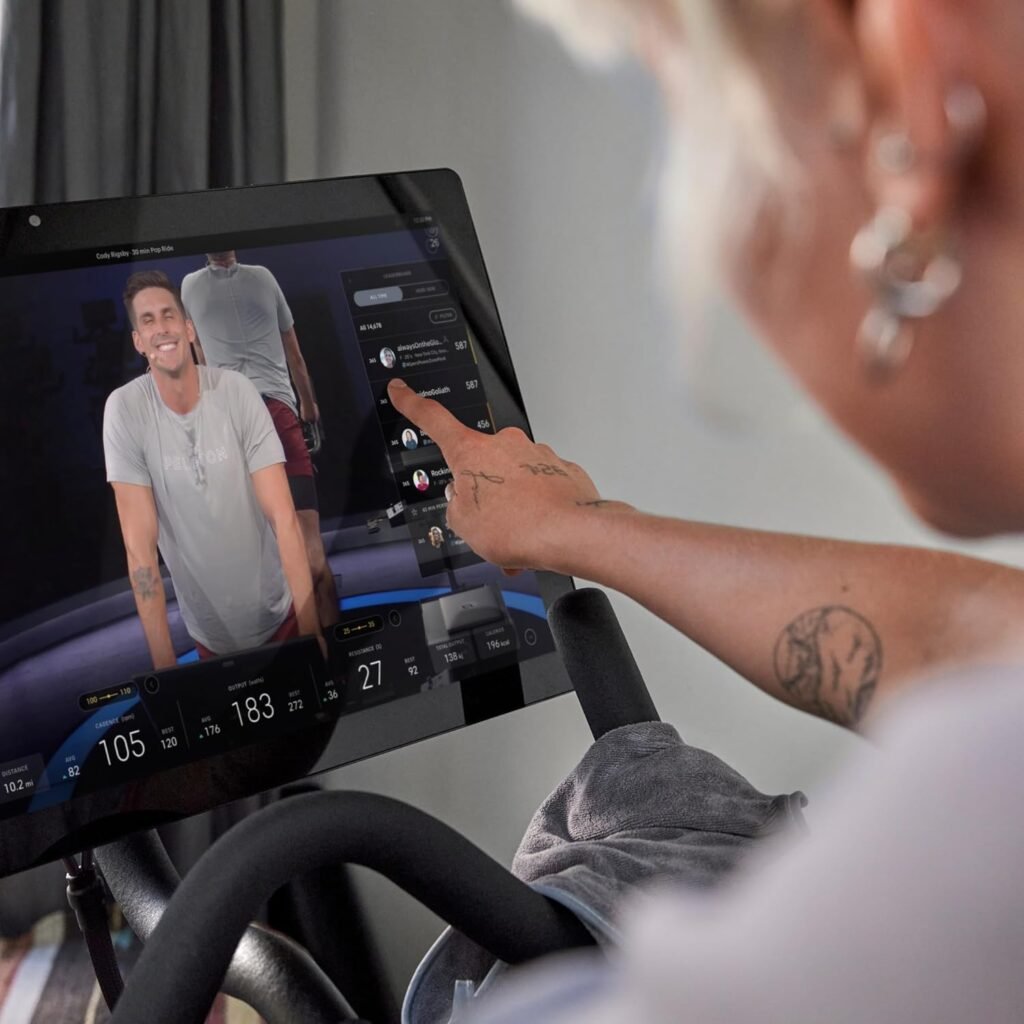 Peloton indoor exercise bikes: A person is using a touchscreen on a stationary bike, engaging with a virtual cycling class displayed on the screen.